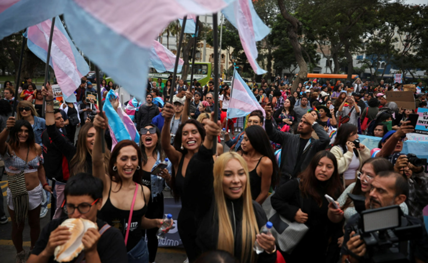 Picture of a protest outside the Peruvian Health Ministry. People are holding trans flags.