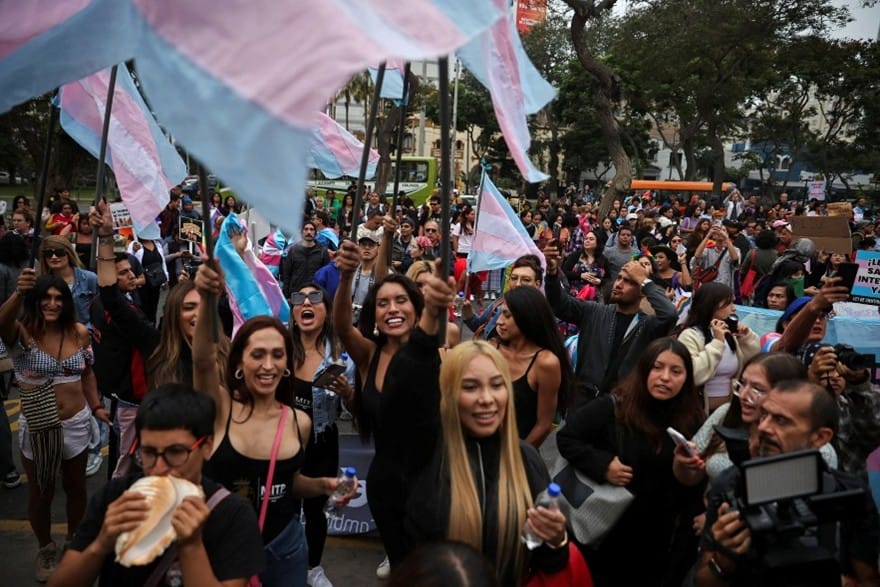 Photo of trans women protesting in Peru. Several trans blue and pink flags are being held.